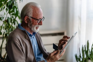 Gözlüklü kıdemli işadamının dijital tablet ve kredi kartı kullanarak portresi 