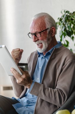Gözlüklü kıdemli işadamının dijital tablet ve kredi kartı kullanarak portresi 