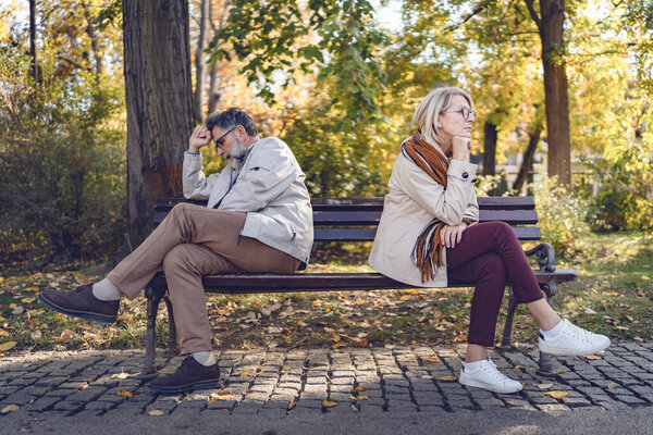 sad senior man and woman sitting in park  