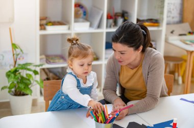 Öğretmen ve küçük kız anaokulunda resim çiziyorlar.