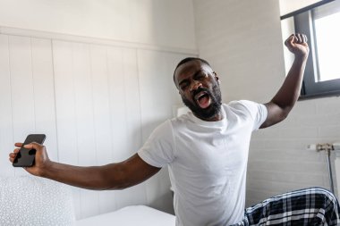 Yatak odasında cep telefonu olan Afrikalı bir adam.