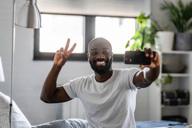 Gülümseyen Afrikalı Amerikalı adam selfie çekiyor ve zafer işareti gösteriyor. 