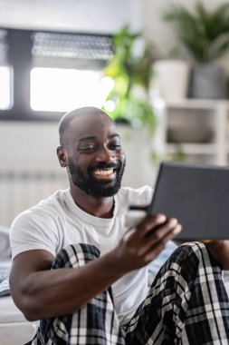 Genç siyah adam tablet kullanırken gülümsüyor ve online alışveriş yapıyor. 