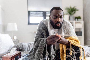 Hasta Afrikalı Amerikalı adam termometreyle yatakta. 