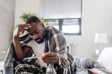 Hasta Afrikalı Amerikalı adam termometreyle yatakta. 