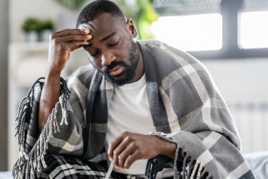 Hasta Afrikalı Amerikalı adam termometreyle yatakta. 