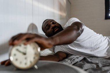Afro-Amerikan adam çalar saatle yatakta.