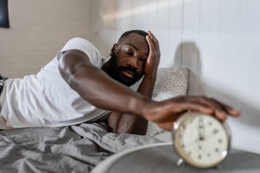 Afro-Amerikan adam çalar saatle yatakta.