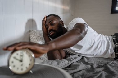 Afro-Amerikan adam çalar saatle yatakta.