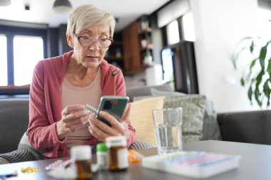 Yaşlı kadın akıllı telefon kullanarak ilaç talimatlarını kontrol ediyor.