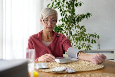Evde tansiyonunu ölçen yaşlı bir kadın var. 