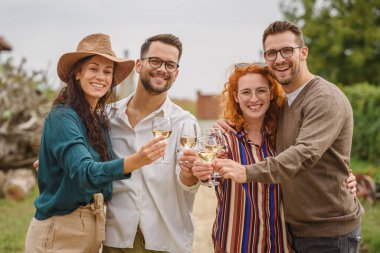 Dışarıda kutlama yapan gülen arkadaşlar bir arada şarap kadehleri tutuyorlar.