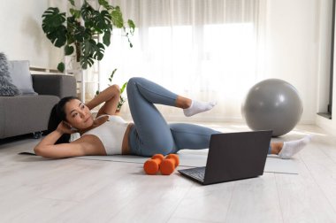 Genç bir kadın spor yapıyor, online spor dersi alıyor. 