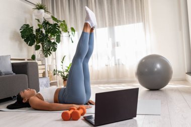 Genç bir kadın spor yapıyor, online spor dersi alıyor. 