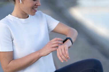 Gülümseyen kadın suyun yanında otururken akıllı bakışlarını kontrol ediyor.