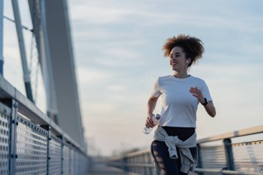 Gündoğumunda modern köprüde koşan genç bir kadın.