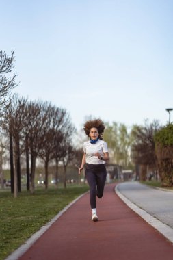 Genç bir kadın sabah vakti açık hava parkı yolunda koşuyor.