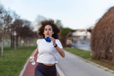 Dışarıda koşan genç bir kadın elinde su şişesi koşu yolu tutuyor.