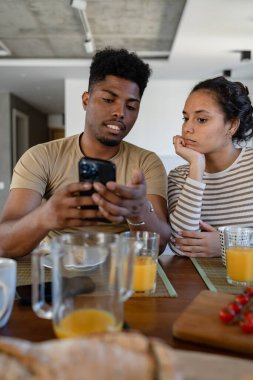 Evde kahvaltıda akıllı telefona bakan bir çift.