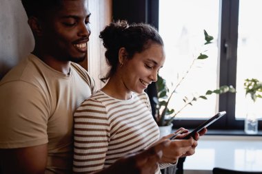 Pencerenin yanında akıllı telefon kullanan gülümseyen çift.