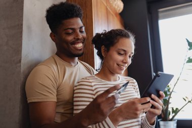 İçerde tablet ve kredi kartı kullanan gülümseyen çift.