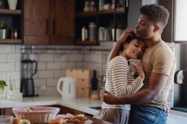 Sıcak mutfakta kahve fincanıyla kucaklaşan çift.