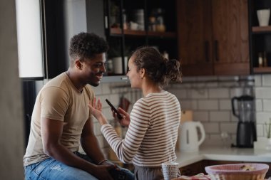 Modern mutfakta konuşan çift akıllı telefon tutuyor.