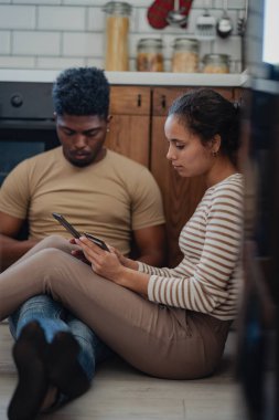 İki yetişkin mutfak zemininde akıllı telefon kullanıyor.