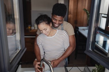 Couple washing dishes together in domestic kitchen