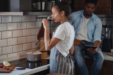 Modern mutfakta yemek pişirirken şarap içen kadın.