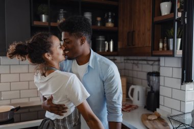 Modern mutfakta tahta dolaplarla kucaklaşan bir çift.