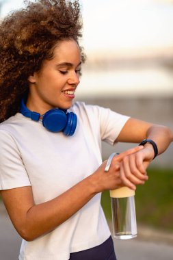 Gülümseyen kadın dışarıda su tutarken akıllı bakışlarını kontrol ediyor.