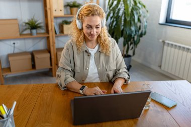 Kadın kulaklıkla çalışıyor ve dizüstü bilgisayar kullanıyor. 