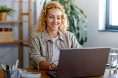 Ofiste dizüstü bilgisayar kullanan gülümseyen genç bir kadının portresi