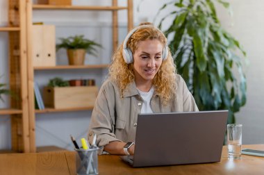 Kadın kulaklıkla çalışıyor ve dizüstü bilgisayar kullanıyor. 