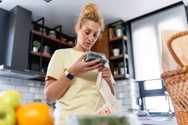 Genç bir kadın mutfaktaki bavulları boşaltıyor. 