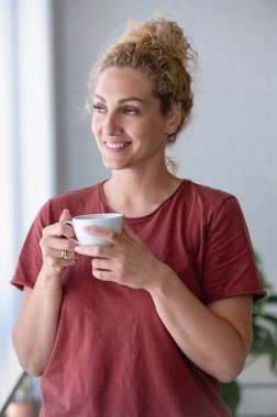 Sarışın genç bir kadın sabah kahvesini evde içiyor.