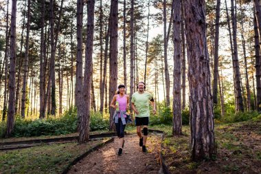 Smiling couple jogging through tall pine forest trail together