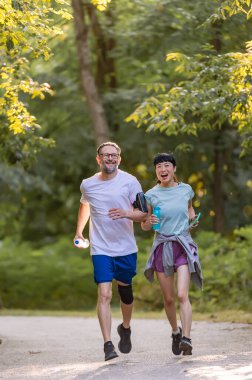 Smiling couple jogging together through sunny green forest trail