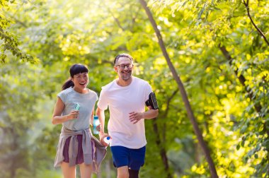 Smiling couple jogging together through sunny green park trail
