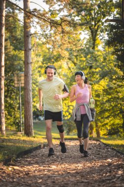 Smiling couple jogging together through sunny green forest trail