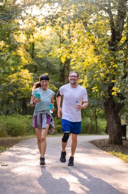 Smiling couple jogging together through sunny green park trail