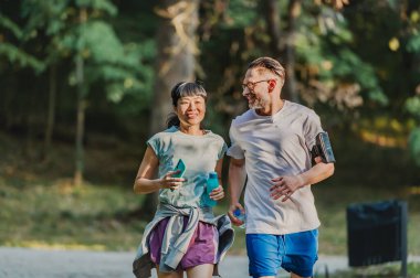 Smiling couple jogging together through sunny green park outdoors