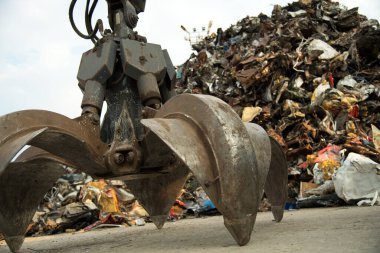 Geniş çaplı bir kazıcı metal geri dönüşüm alanında çelik bir kazıda çalışıyor. Endüstriyel metal geri dönüşümü - seçici odak, kopyalama alanı