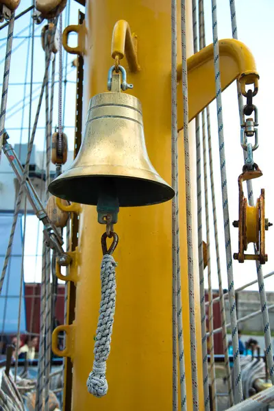 Eski paslı bir çapadan sallanan küçük bir gemi zili. Deniz arka planı. Seçici odak.