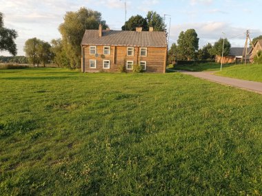 Çayırdaki eski ahşap ev, ağaçlar ve gökyüzü arka planı. Dusetos kasabası, Litvanya 'daki ev.
