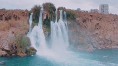 Muhteşem doğal manzara. Fırtınalı bir şelalenin kayadaki yavaş çekimi. Sahildeki otel. Akan su. Hava aracı görüntüleri. Yüksek kalite 4k görüntü
