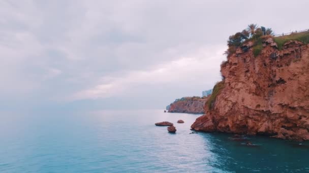海岸沿いの青い海の上を飛行します 赤い岩だ 遠くの住宅ビル 空中ドローンビデオ4Kビデオ 高品質4K映像 — ストック動画