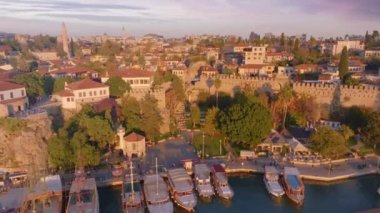 Rıhtımdaki evlerin, teknelerin ve yatların çatılarından tepedeki manzara. Gün batımı. Deniz Burnu. İHA video görüntüleri. Yüksek kalite 4k görüntü