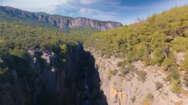 Hava aracı video görüntüleri. Dağ nehrinin en üst manzarası. Yeşil ağaçlar ve kayalıklardaki çalılar. Mavi gökyüzü beyaz bulutlar. Yüksek kalite 4k görüntü